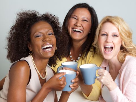 Three woman holding mugs and laughing. 