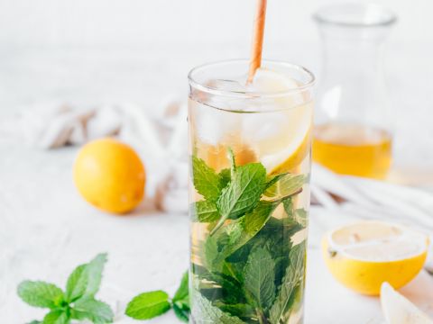 Glass of tea with mint leaves and lemon slices on a table with more mint leaves and lemon slices. 