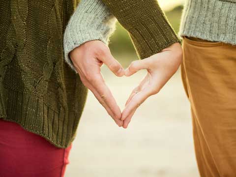 A close up image of a couple's hands forming a heart.