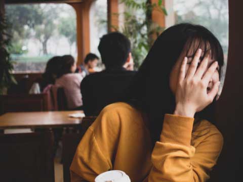 Women holding hand over face in coffee shop. 