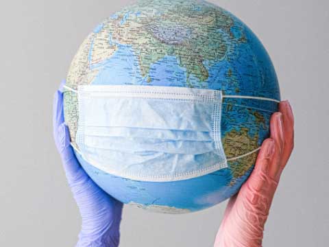 Gloved hands holding up globe with face mask.