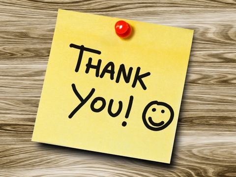 'Thank You' written on yellow post-it note with a smiley face and attached to a wooden background with a thumb tack. 